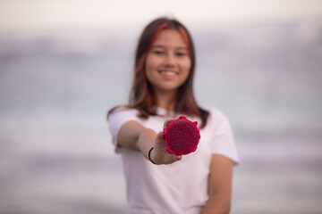 Portrait of girl holding half a dragon fruit in front of her. Selected focus on red dragon fruit. Blurred female.