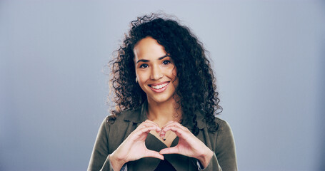 Woman, portrait and heart hands with love sign, gesture or romance on grey background space in studio. Happy person, smile and emoji or shape, symbol and kindness for opinion and support mockup