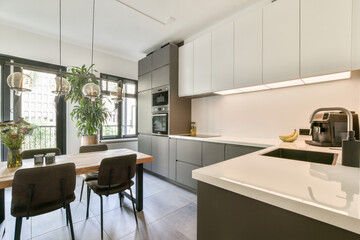 A sleek modern kitchen featuring minimalist cabinetry and stylish furniture, illuminated by natural light from large windows, creating a welcoming atmosphere.