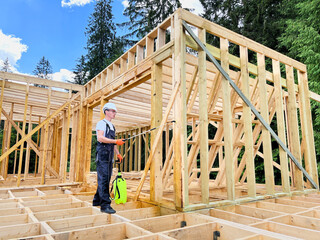 Laborer constructing wooden frame house near forest. Man treating woods, applying fire retardant...