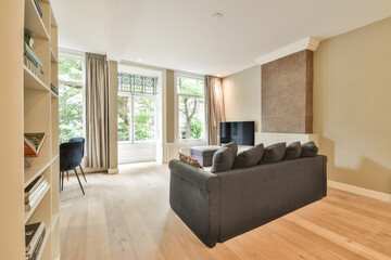 A stylish modern living room featuring large windows that allow plenty of natural light. The decor includes a cozy couch and contemporary furnishings.