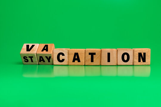 turned wooden blocks with vacation and staycation words symbol isolated on green background