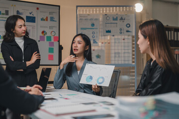 Group of young asian businesswomen discussing new project during briefing in boardroom, analyzing financial charts and planning marketing strategy together in office