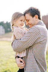 Fototapeta premium Smiling dad hugs little girl in his arms, touching their foreheads with her