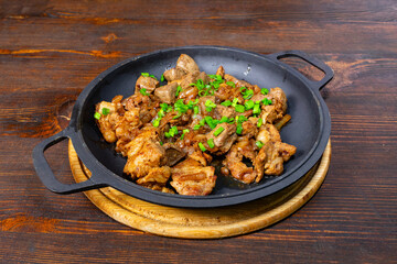 Sizzling platter of seasoned meat with green onions on wooden table