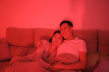Asian couple relaxing and embracing on sofa in red light
