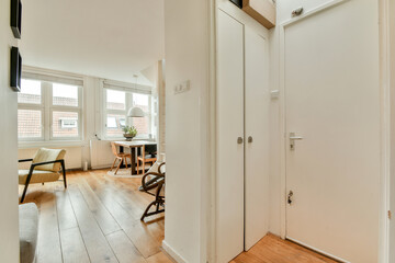 A well-lit modern interior hallway showcasing wooden flooring and a glimpse of a dining area with a round table and stylish chairs.