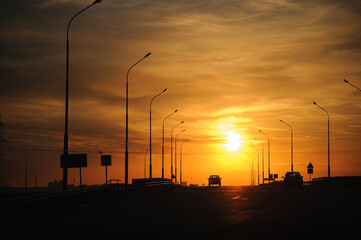 Fiery sunset at a road junction. Silhouette of a car and lanterns against the backdrop of the...
