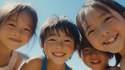 日本の小学生・幼稚園児・保育園児4人がカメラを覗き込んで笑っている写真　背景青空　夏