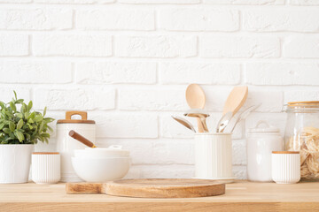 Table top with dish podium board on background of white brick wall and kitchen utensils