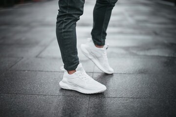 Man wearing white sneakers and jeans standing on city street
