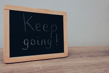 Writing Keep going on chalkboard. Keep Going text in a motivational chalk font. Handwritten text on a blackboard