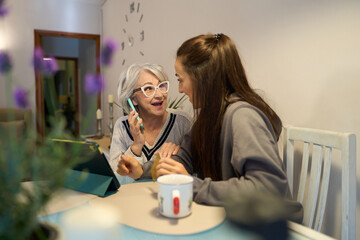 Senior woman sharing news on phone with caregiver at home