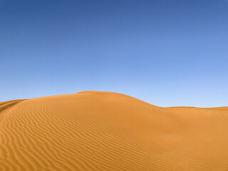 A sand dune against a clear blue sky. Waves of sand. Natural background. Сopy space.