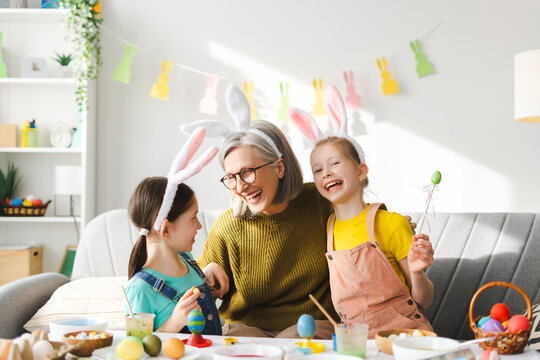 Grandmother and granddaughters painting easter eggs wearing bunny ears