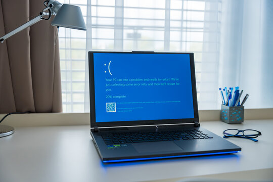 Prague, Czech Republic - September 11, 2024: A laptop displays the blue screen of death while in use at a home office desk, signaling a system crash. The workspace is organized near the window.
