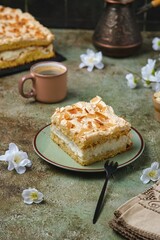 Norwegian dessert, sliced best cake with meringue, almonds and custard on a dessert plate on a green concrete background. Norwegian cuisine.