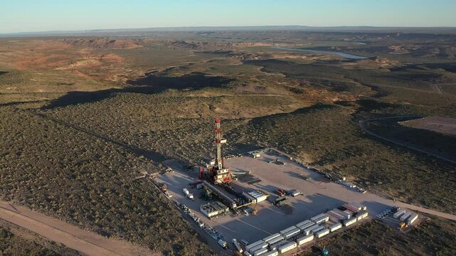 An oil field in the middle of a Patagonian landscape with rivers, mountains and hills. A drilling rig for fracking and oil and gas.