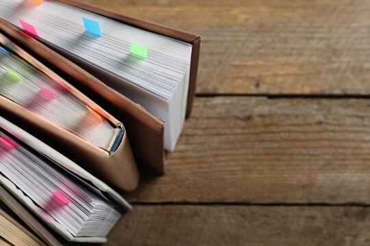 Books with colorful tabs on wooden table, above view. Space for text