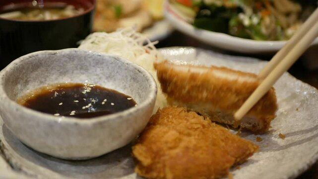 close up selective focus to a plate of crispy deep fried pork or tonkatsu, japanese food while hand using chopstick to pick up a pice of fried pork from a plate in lunch dinning restaurant time
