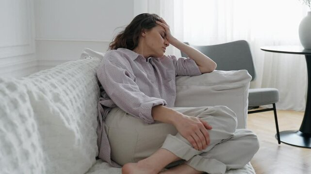 A young woman is suffering from a headache while sitting on the couch in the living room