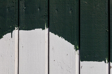 A close-up of painted wooden planks on a building facade, with uneven white and green layers revealing brush marks and imperfect coverage from an inexperienced paint job