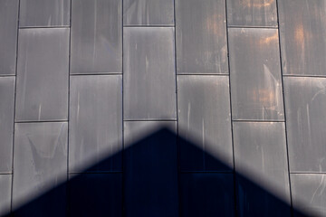 A sharp triangular roof shadow cuts across the rectangular metal facade of a building, creating a...