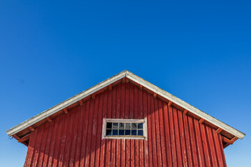 The upper section of an old barn with a central window sits perfectly framed against a clear blue sky, showcasing rustic textures and timeless symmetry.