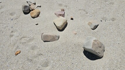 Scattered stones and rocks on sandy ground under bright sunlight, natural outdoor background
