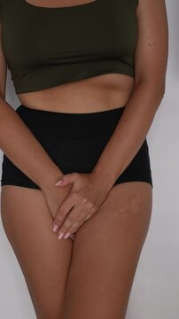 Young woman holding her crotch with her hands, suffering from cystitis or wants to pee on a dark grey background. Gynecological problems, genital tract infections. Vertical video
