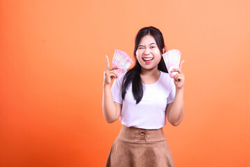 Woman winking and holding two bundles of Indonesian Rupiah banknotes against orange backdrop