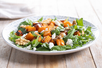 Pumpkin salad with arugula, walnuts and feta cheese on wooden table