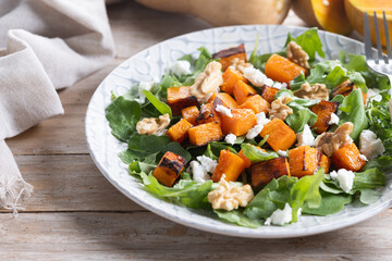 Pumpkin salad with arugula, walnuts and feta cheese on wooden table