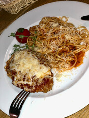 Close-up of a serving of spaghetti with a tomato sauce, garnished with Parmesan cheese, and accompanied by a portion of chicken Parmesan topped with melted cheese, creating a savory Italian meal.