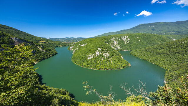 A canyon on the Vrbas River in Bosnia and Herzegovina, Europe. Lush green river valley curves dramatically between forested hills under a clear blue sky, creating a scenic and natural landscape.