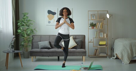 A woman is practicing yoga in her modern living room to improve her strength and wellness