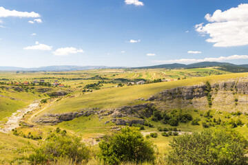 Fototapeta premium View of country in Bosnia and Herzegovina, Europe. Scenic landscape panorama of rolling hills and fields under a blue sky with scattered clouds, offering a peaceful, natural countryside vista.