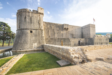Ston, historic town in Peljesac peninsula in Croatia, Europe. Ancient stone castle with a round tower, surrounded by a moat and grassy area under a bright blue sky with scattered clouds. © Viliam