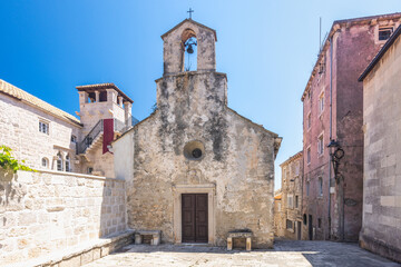Fototapeta premium Korcula town in island of Korcula in Adriatic sea in Croatia, Europe. Historic church with aged stone facade and bell tower, set against a bright blue sky in a charming European town.