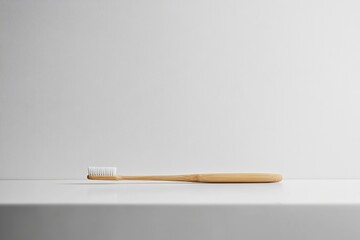A sustainable bamboo toothbrush with soft bristles rests on a pristine white surface against a textured white wall.