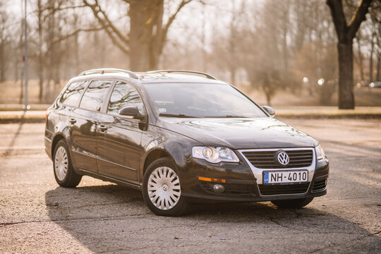 A black Volkswagen Passat station wagon is parked outdoors on a sunny day with a blurred background of trees and soft golden light.