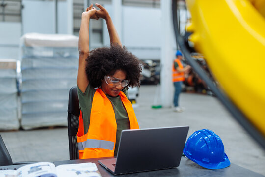 Female engineer stretching while working on laptop in factory