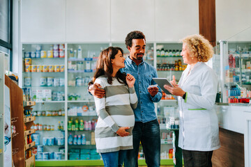 Cheerful pregnant woman and husband talking with pharmacist.