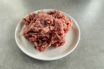 Raw ground meat on a white plate, gray countertop