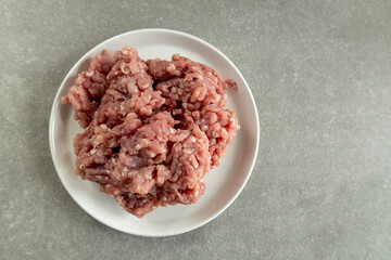 Raw ground meat on a white plate, gray countertop, top view