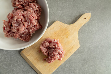 Raw ground meat on a wooden cutting board and in a bowl  