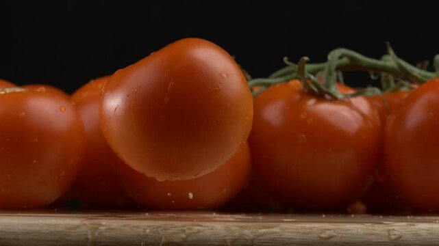Single tomato falls into wooden surface in ultra slow-motion with water splashing at 1000 fps with multiple tomatoes on display in background