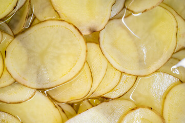 Close-up view of thinly sliced potatoes submerged in water, showcasing their pale color and texture. Ideal for culinary, cooking, or food preparation themes