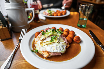 Chicken steak with ham, cheese, green shoot and fried croquettes with spicy sauce in white plate, restaurant table.
