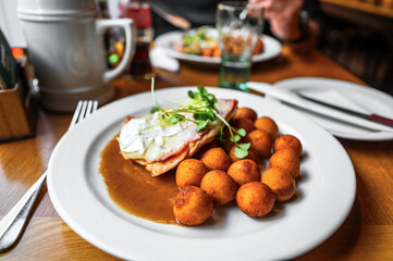 Fried croquettes, chicken steak with ham and cheese, green shoot and sauce on restaurant table.